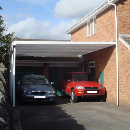 SW Plastic Carports. Two cars parked at the side of a house underneath a carport.