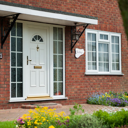 SW Plastic uPVC Doors. white uPVC door on a red brick house with a beautiful garden.